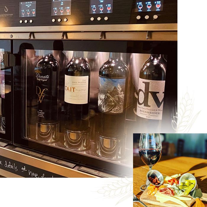 Wine bottles in a dispenser, Nichole's Fine Pastry plate, and red wine on a wooden table.