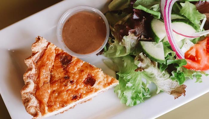 A slice of quiche with mixed green salad, perfect for any event space or cozy bakery setting.