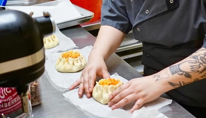 At Nichole's Fine Pastry, a chef in dark coat fills dough on parchment in the kitchen.