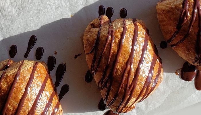 Three croissants drizzled with chocolate at Nichole's Fine Pasty, glowing in café sunlight.