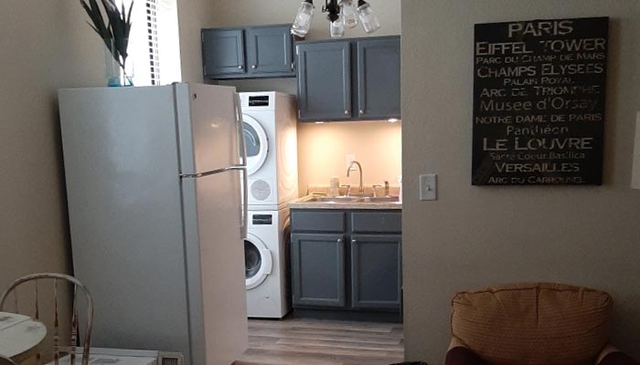 Small kitchen with gray cabinets, stacked washer-dryer—ideal for catering or event space needs.