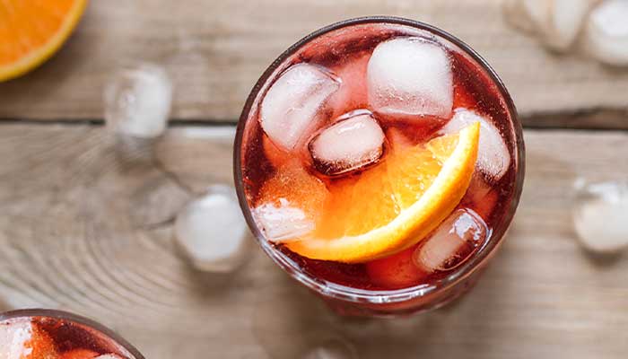 A glass of iced red drink garnished with an orange slice at a cozy café on a wooden surface.