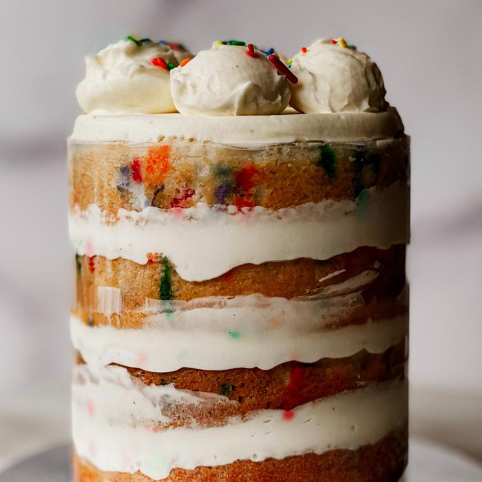 A tall café confetti cake with white frosting and three cream dollops topped with sprinkles.