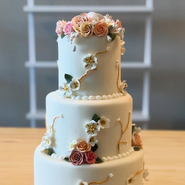 Three-tiered white cake from our bakery, adorned with pastel fondant flowers and gold vines.